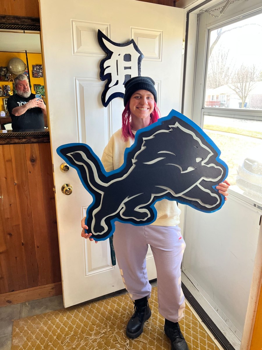 Customer holding a custom black and blue Detroit Lions logo cutout in front of a Tigers D on the door