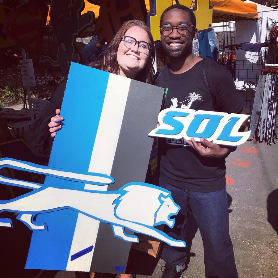Custom retro Detroit Lions cutout and a SOL sign held by customers at an art fair