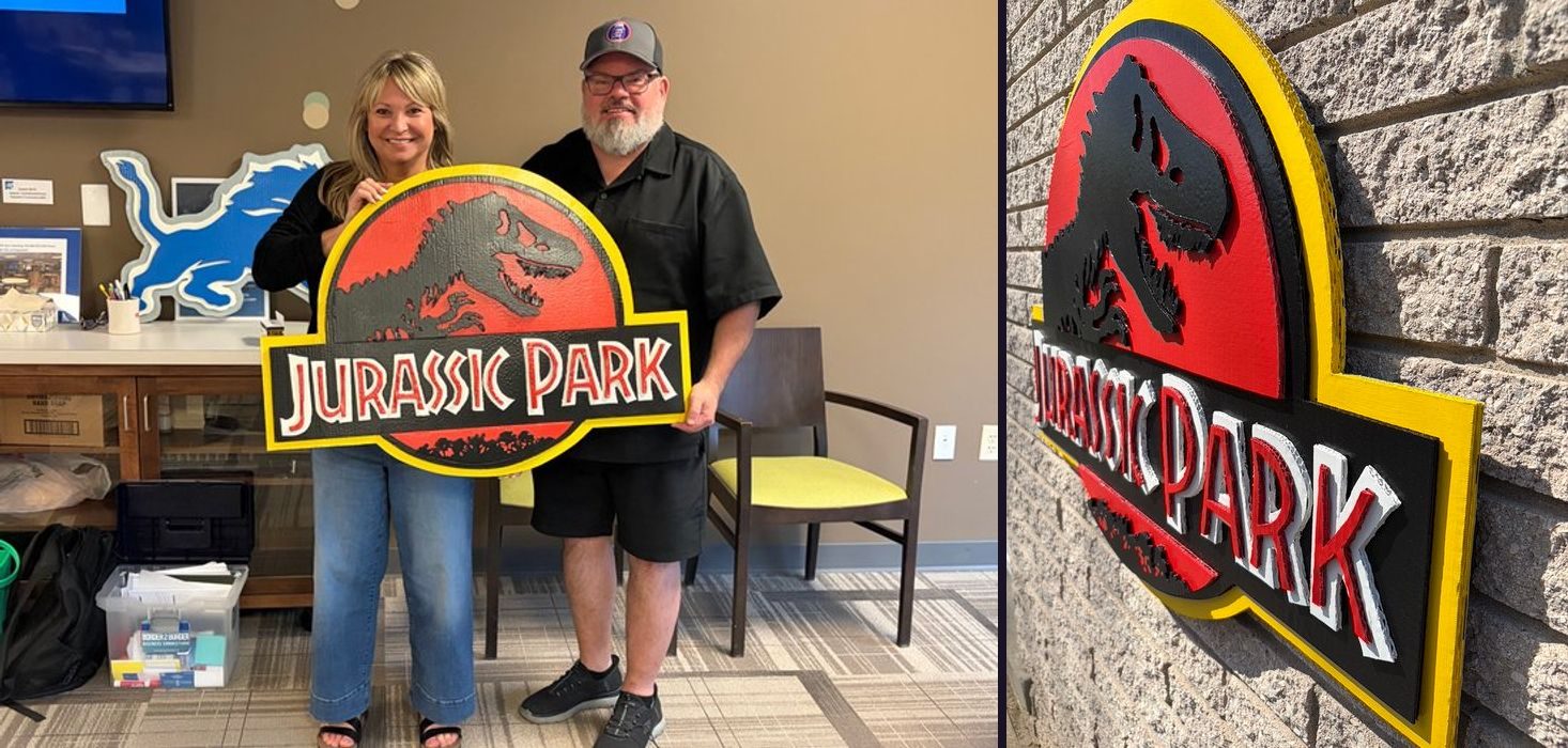 Jurassic Park fan art logo cutout in red, black, yellow and white, held by customers, and an angled view on a brick wall showing the layers