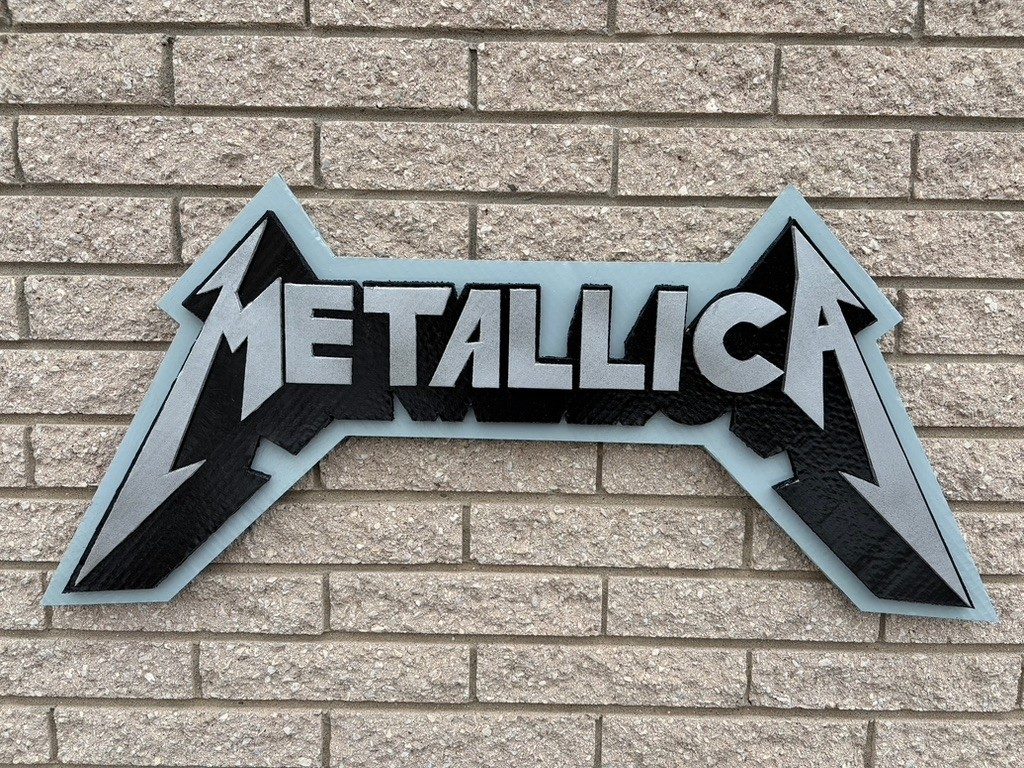 Custom Metallica logo cutout in black and silver with a pale blue backing, on a brick wall