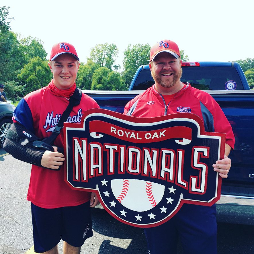 Custom Royal Oak Nationals baseball logo cutout in red, navy and white, held by two team members