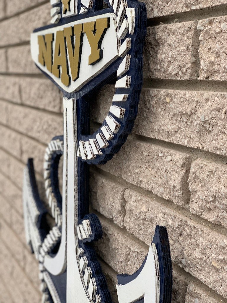 Angled close-up of the custom Navy anchor cutout in navy, white and gold on a brick wall, showing the layered cardboard rope