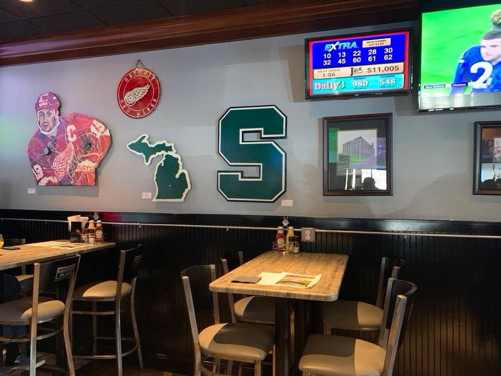 Custom Michigan State block S and Michigan state cutouts on a sports bar wall beside a Detroit Red Wings sign and a hockey player portrait
