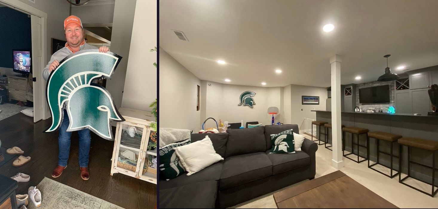 Customer holding a custom Michigan State Spartan helmet cutout, and the helmet hung on the wall of a finished basement lounge