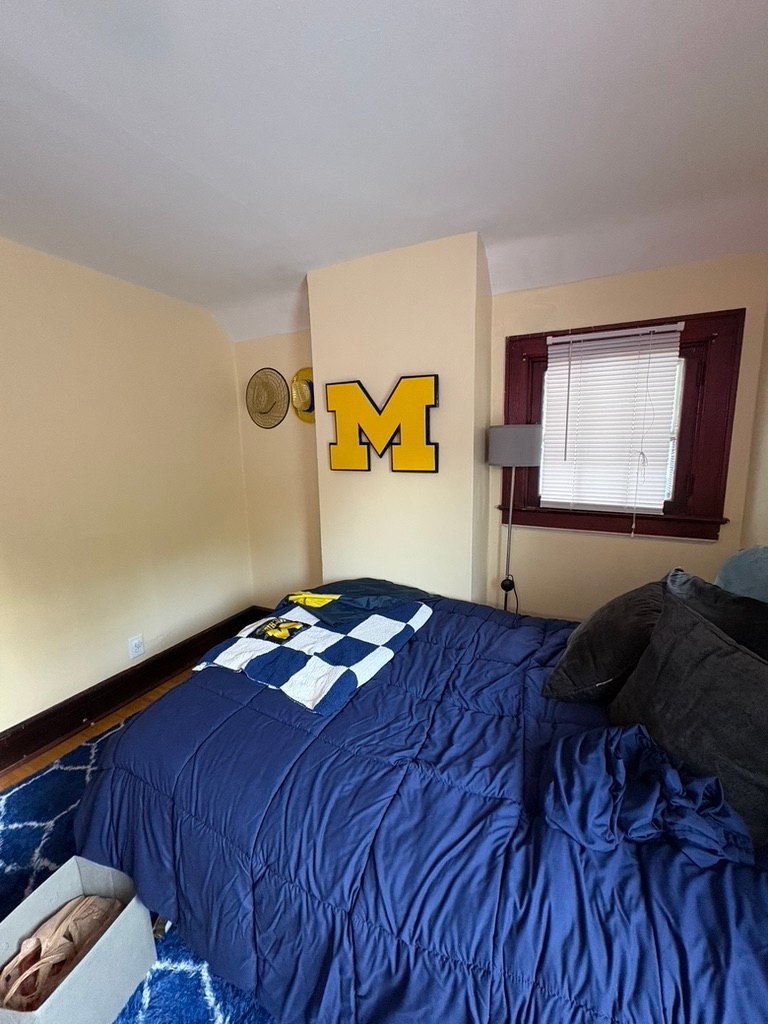 Custom maize Michigan block M cutout with navy trim on the wall of a bedroom above a blue bed with a Michigan blanket
