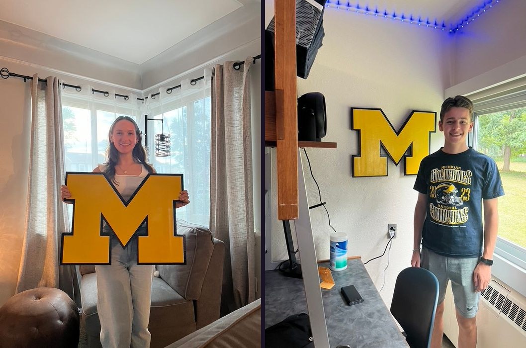 A graduate holding a custom maize Michigan block M cutout in her living room, and a student standing beside the same M hung in his dorm room with blue LED lights