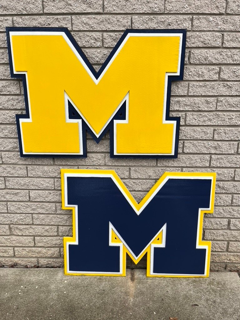 Custom maize and navy Michigan block M cutouts stacked on a brick wall