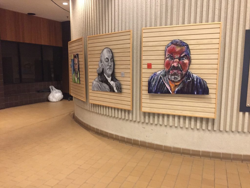 Cardboard portraits of Benjamin Franklin and Jeremy Rheault on wood slat panels
