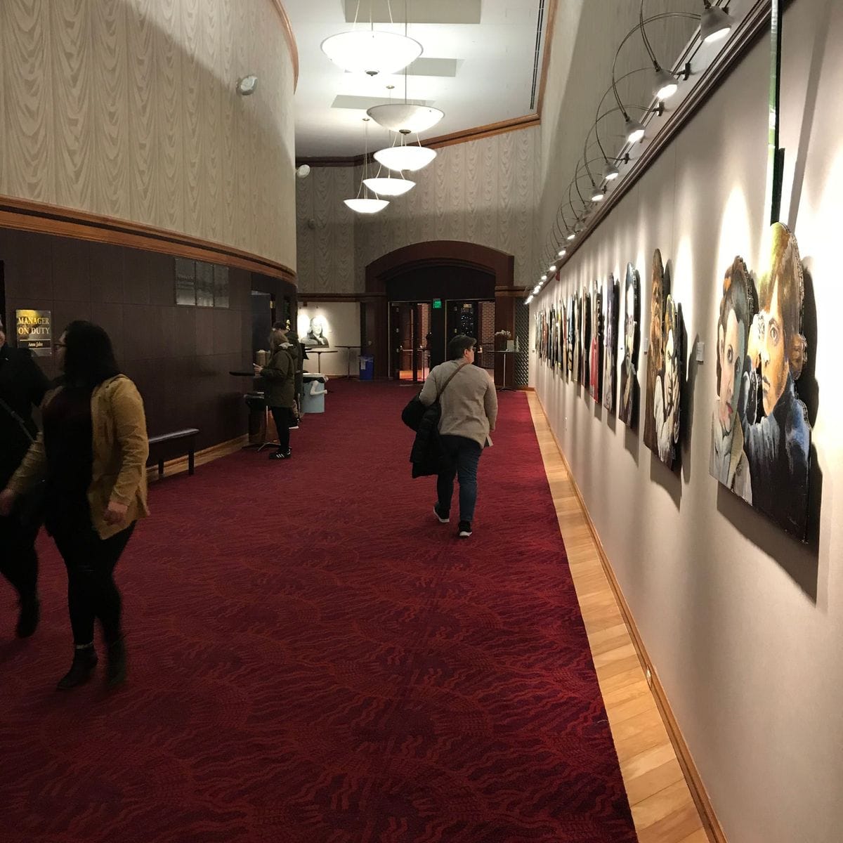 Visitors walking down the gallery hallway past the portraits