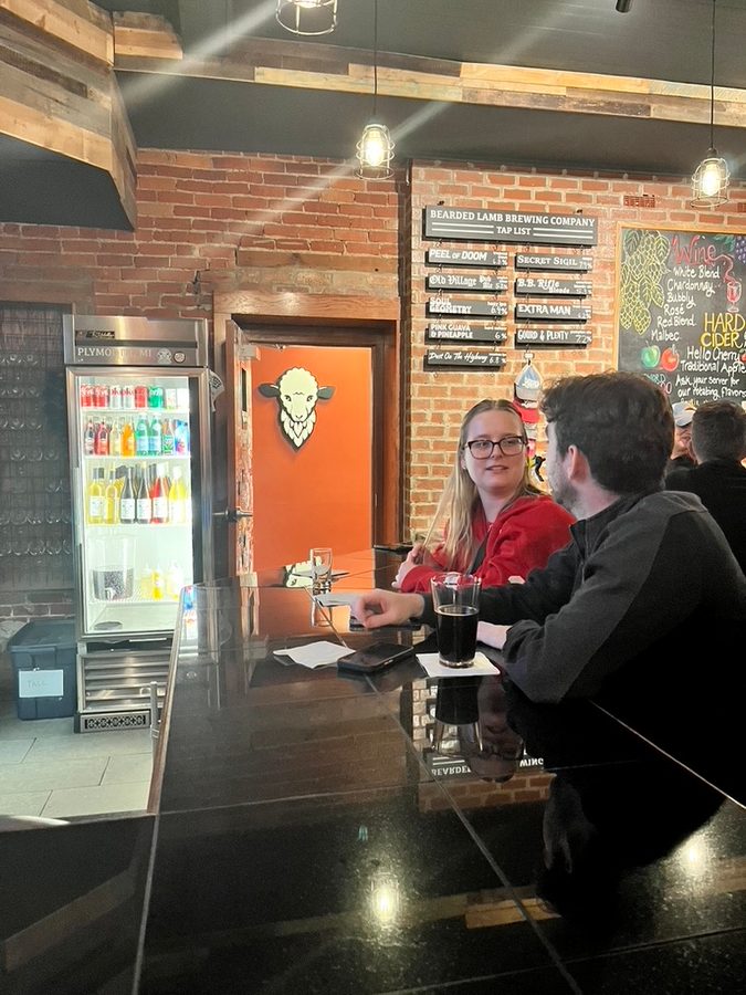 Customers at the bar at Bearded Lamb Brewing Co. with the sheep logo on the orange door and the tap list behind them