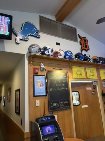 Detroit Lions and Detroit Tigers D logo cutouts hanging above a shelf of football helmets at Crow’s Nest in Canton