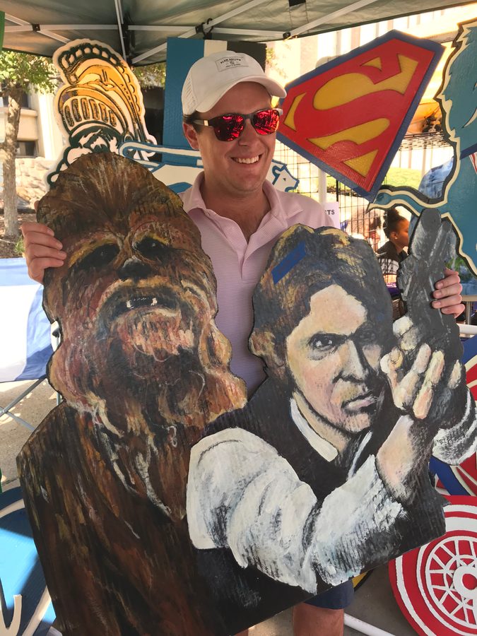 A customer holding hand-painted cutouts of Chewbacca and Han Solo at the booth