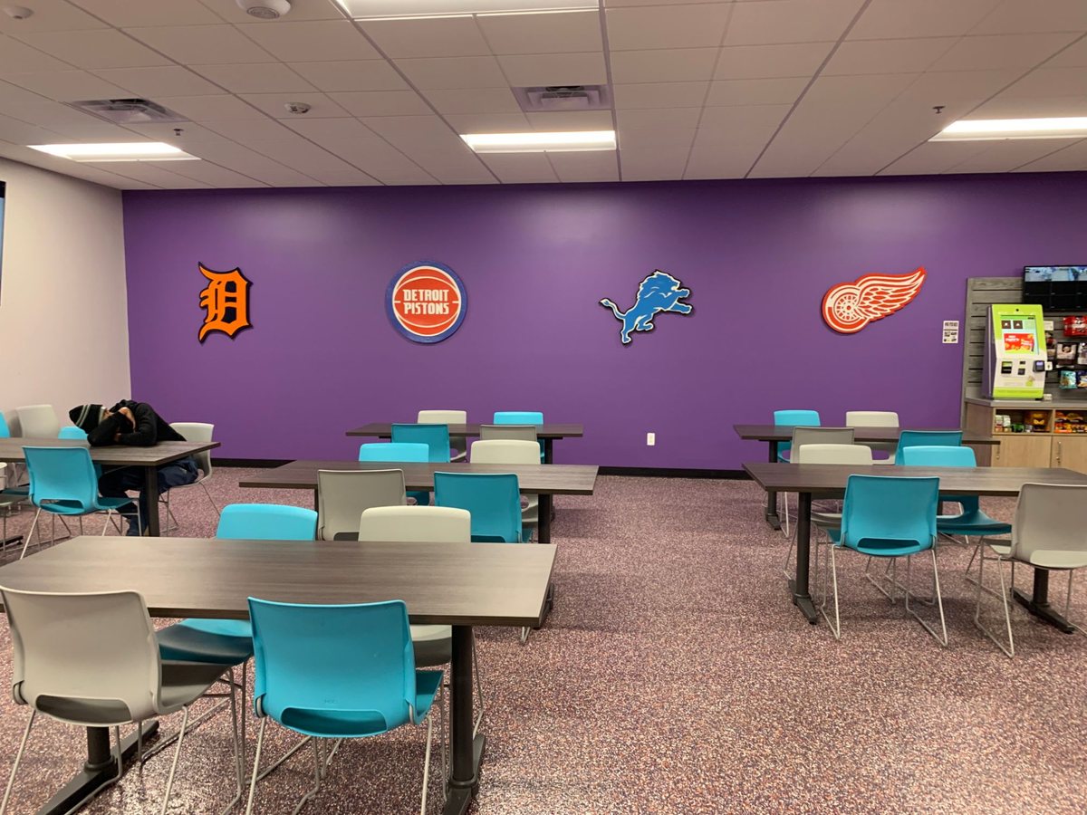 Break room at FedEx Ground with Tigers D, Pistons, Lions and Red Wings logo cutouts on a purple wall above tables and chairs