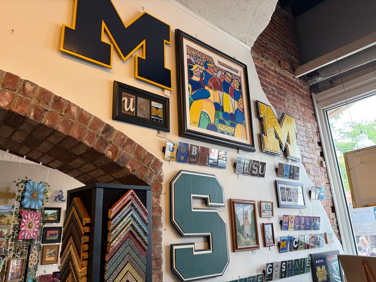 Michigan block M, yellow M and Michigan State S logo cutouts on the brick and plaster wall at Frame Works with framing samples and cards