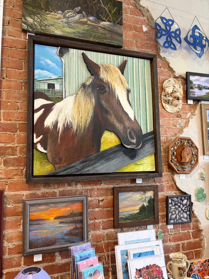 Finn, a painting of a chestnut horse with a pale mane, in a dark Frame Works frame on the brick wall among other framed art