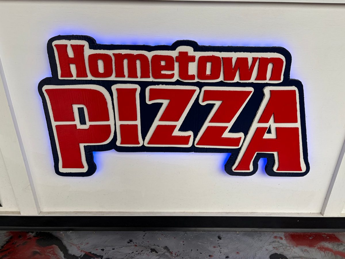 Straight-on view of the layered red, white and navy Hometown Pizza sign with a blue glow behind it