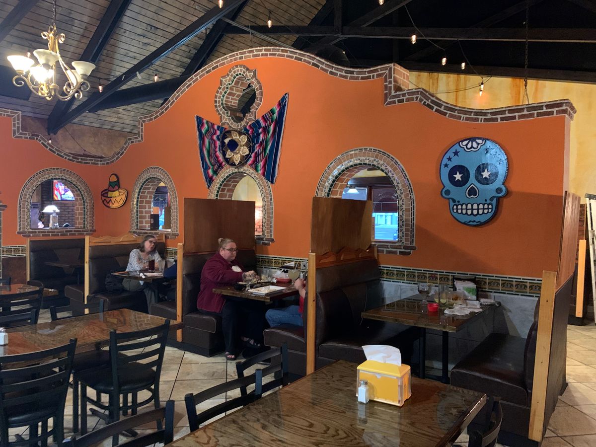 Dining room at Los Amigos with the blue sugar skull and a winged mural on the orange wall