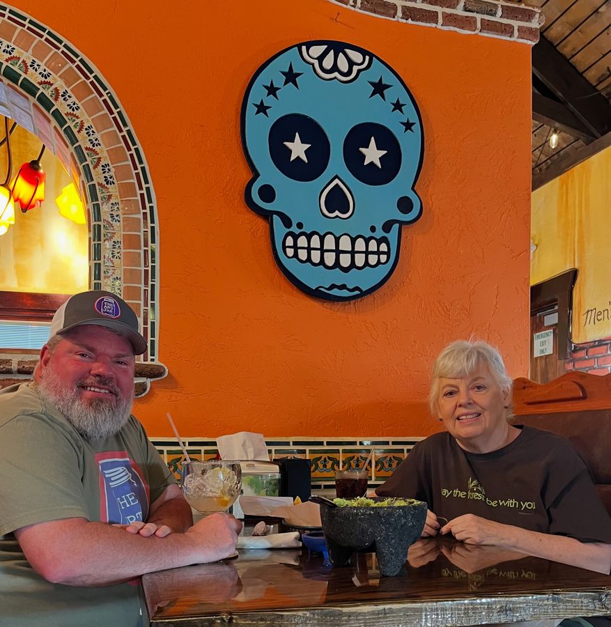 Two customers seated at a table at Los Amigos under the hand-cut blue sugar skull