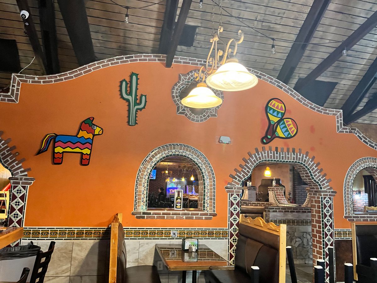 Orange wall at Los Amigos with a hand-cut piñata, cactus and maracas above arched brick windows