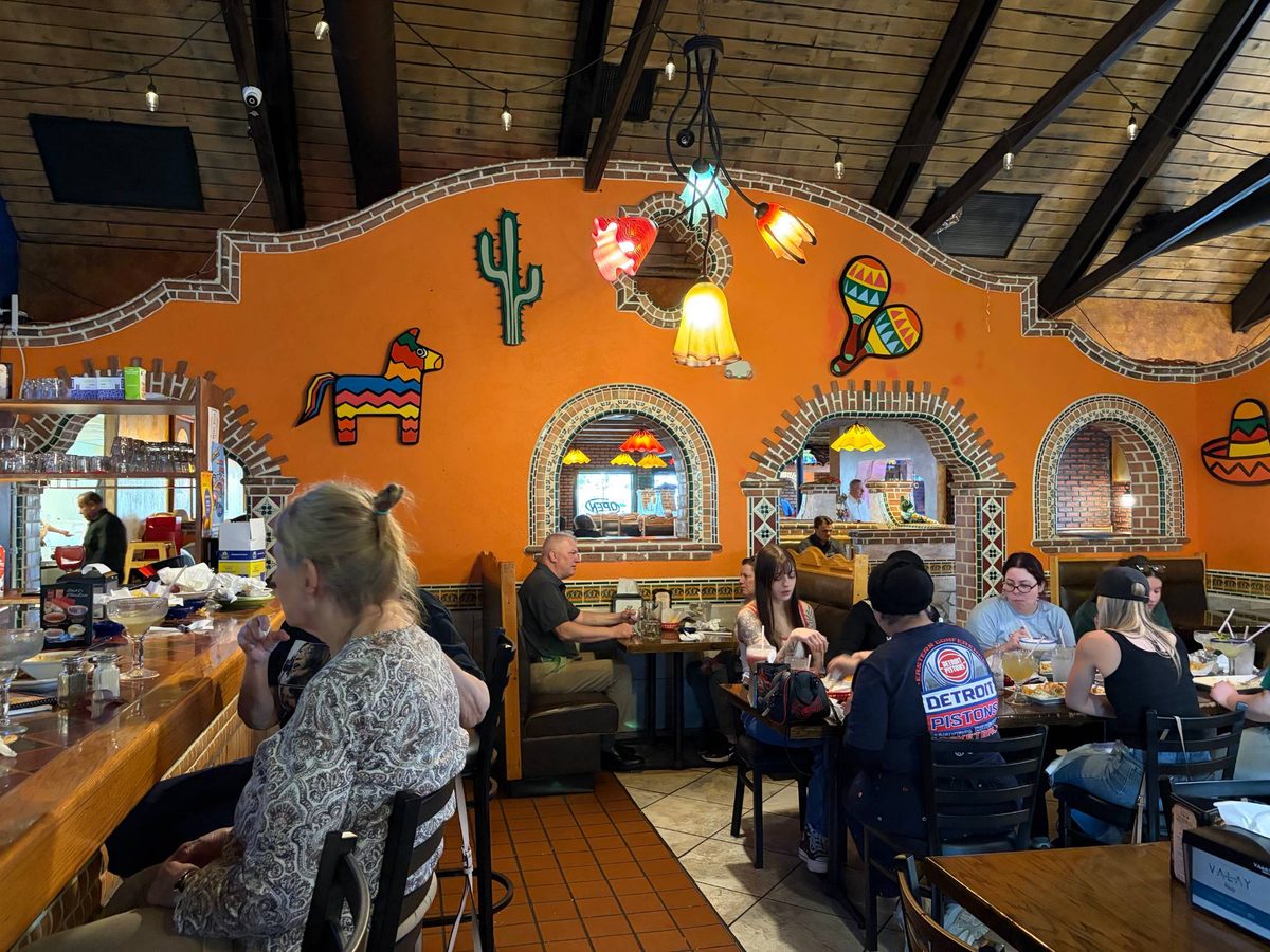 Diners at tables in front of the orange wall at Los Amigos with the piñata, cactus, maracas and sombrero