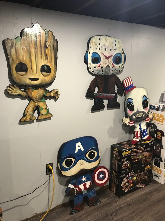 Four hand-cut and hand-painted Funko-style cutouts, Groot, Jason Voorhees, Captain America and Captain Spaulding, on the wall at Popgodz