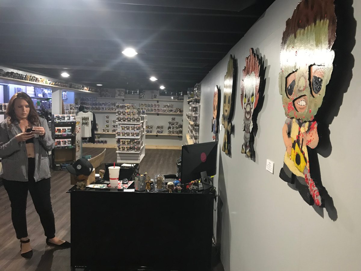 Popgodz shop interior with a customer standing in front of the counter and the Funko-style cutouts on the wall behind