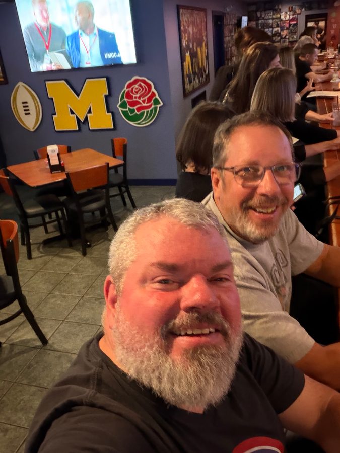 Jeremy Rheault taking a selfie with a customer, the Michigan M and rose on the wall behind