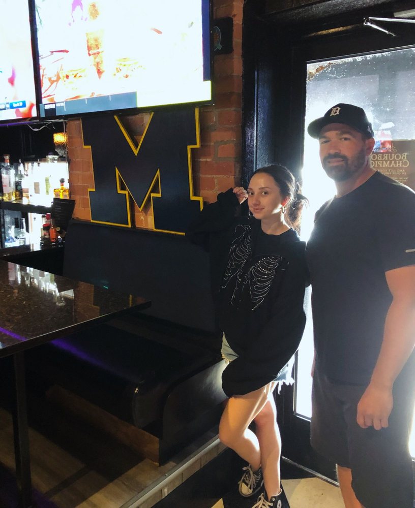 Michigan block M logo cutout on the brick wall above the bar at Sidecar Slider Bar in Plymouth, with two people standing beside it