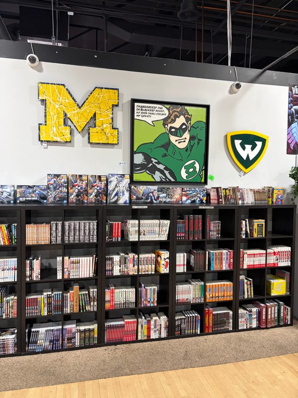 Green Lantern hanging on the wall at State of Comics beside the Michigan M and Wayne State logos