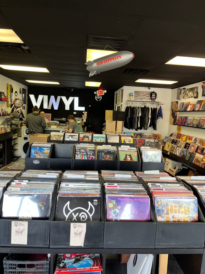 Inside Vinyl People Records, with a VINYL sign, a blimp overhead, record bins and album pieces on the walls