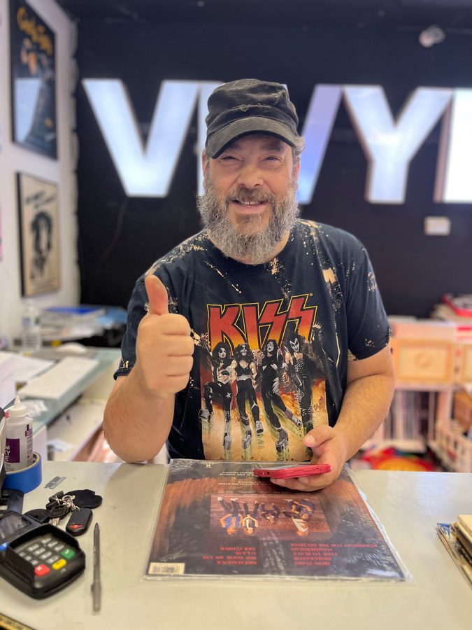 A smiling man in a KISS shirt giving a thumbs up at the counter at Vinyl People Records with a record in hand