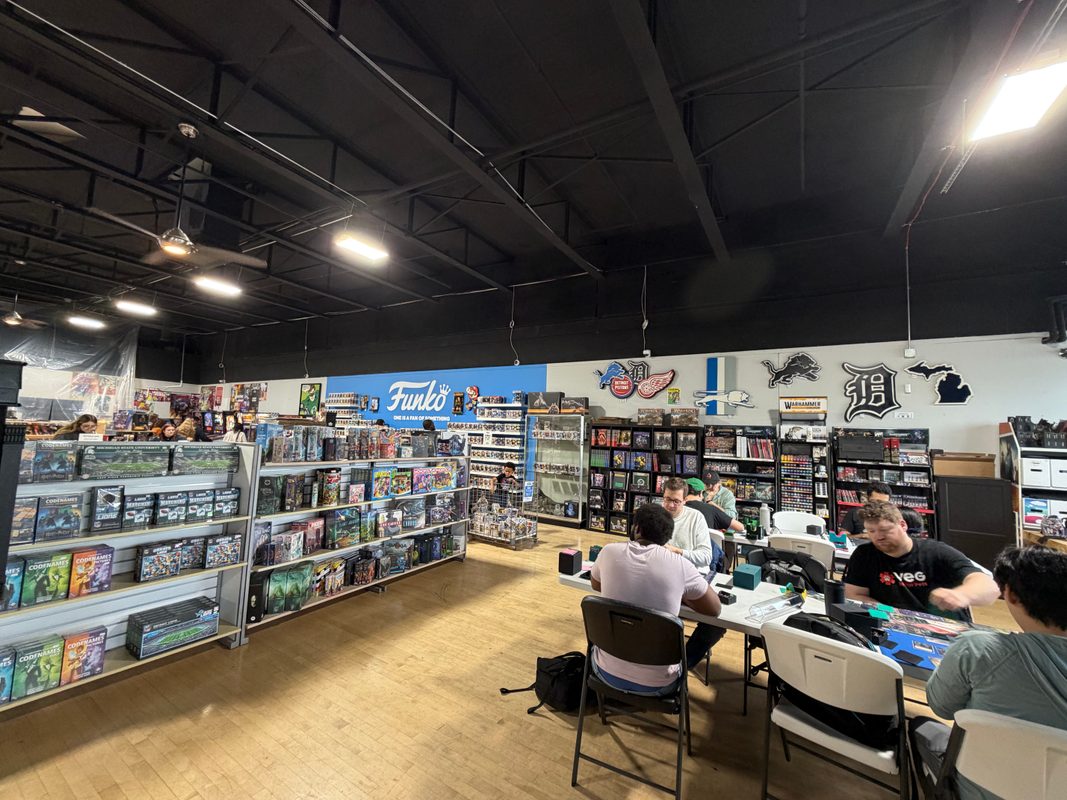 Customers playing at the game tables in State of Comics, with the Michigan logos on the back wall